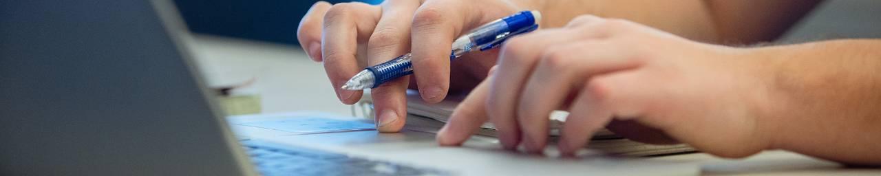 手握蓝色机械铅笔，在笔记本电脑键盘上打字